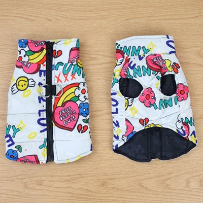 Deux manteaux chien colorés à motifs cartoon avec fermeture zippée et doublure noire posés sur une surface en bois.