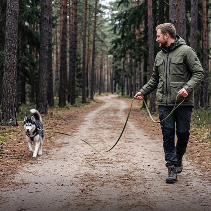 Personne tenant une longe pour chien verte attachée à un husky sur un chemin forestier.